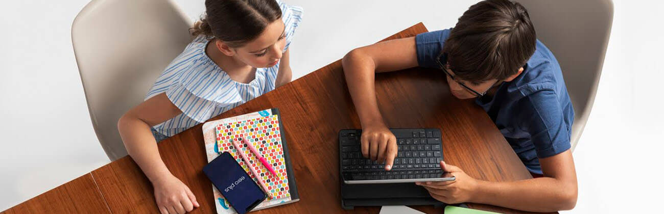 two kids sitting at table using devices