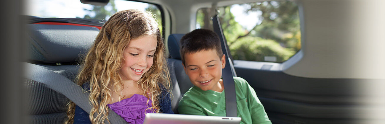 two kids in a car watching tv on their tablet