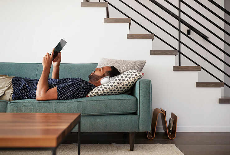 man lying on sofa with tablet and headphones researches internet options